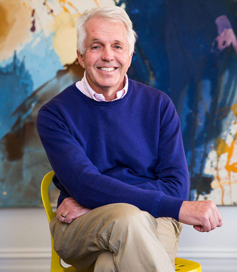 Managing Director, Nigel Dickson, sitting on yellow chair with bright painting in the background